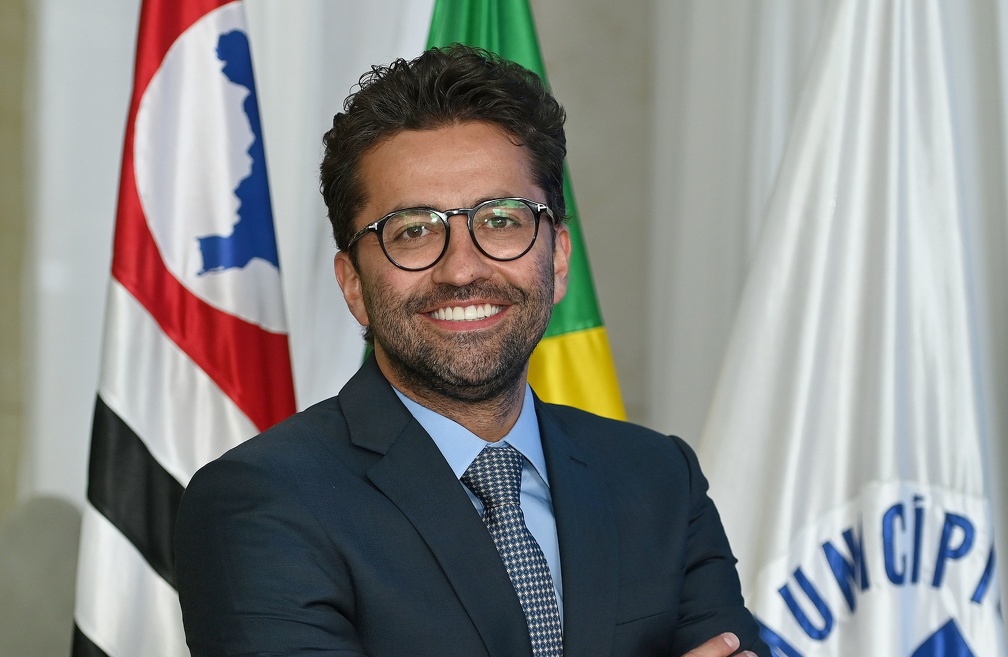 Fotografia do presidente da EMDEC, Vinícius Issa Lima Riverete, com as bandeiras de Campinas e do Brasil ao fundo