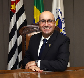 Fotografia do prefeito Dário Saadi, sentado, com as bandeiras de Campinas, do Estado de São Paulo e do Brasil ao fundo