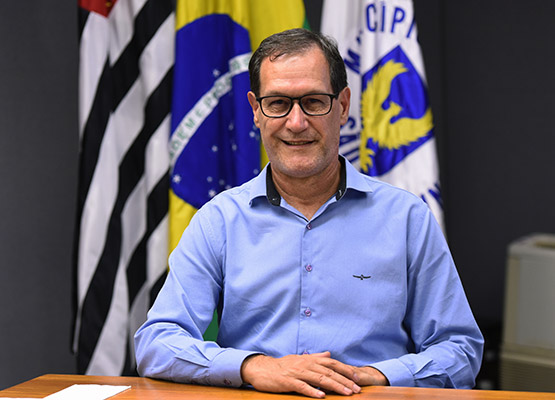 Fotografia do presidente Marionaldo Fernandes Maciel, sentado, com as bandeiras de Campinas, do Estado de São Paulo e do Brasil ao fundo.