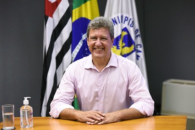 Fotografia do secretário André von Zuben, sentado, com as bandeiras de Campinas, do Estado de São Paulo e do Brasil ao fundo