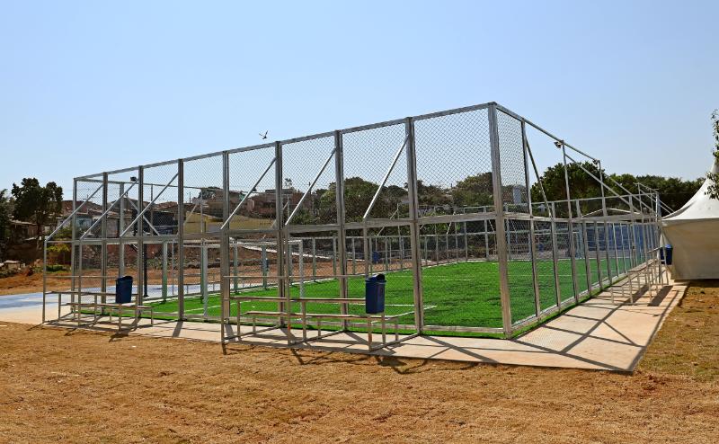 O campo de futebol society é em grama sintética e cercado por alambrado