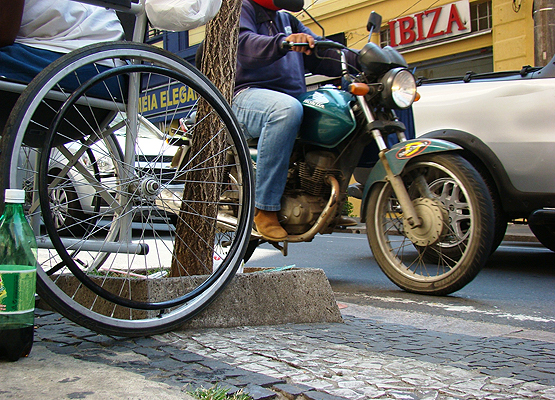 Imagem de uma cadeira de rodas, uma moto e uma rua com trânsito intenso
