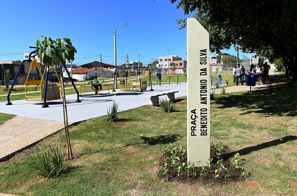 Imagem mostra o totem com o nome da praça Benedito Antonio da Silva com a quadra de esportes ao fundo